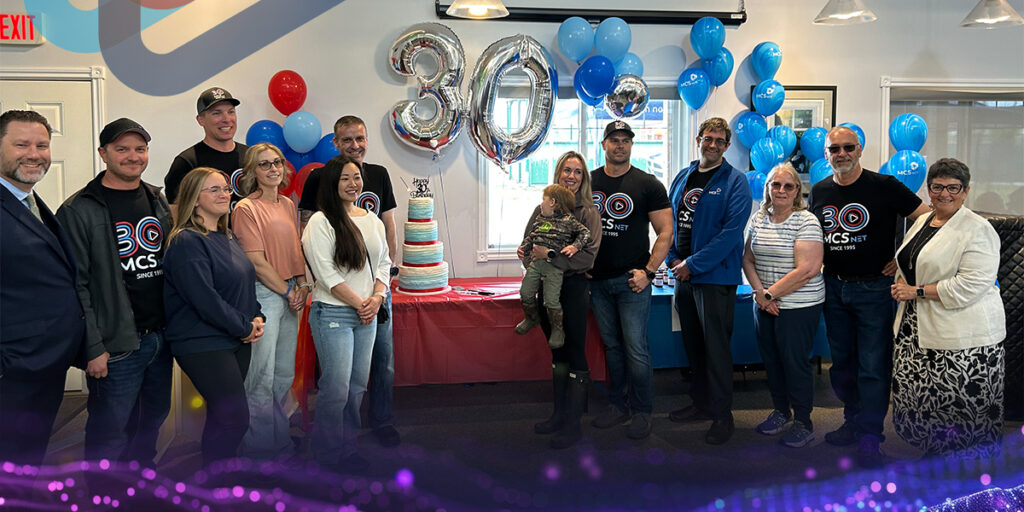 Picture of the local family owners of MCSnet and invited dignitaries in front of the 30th anniversary cake.