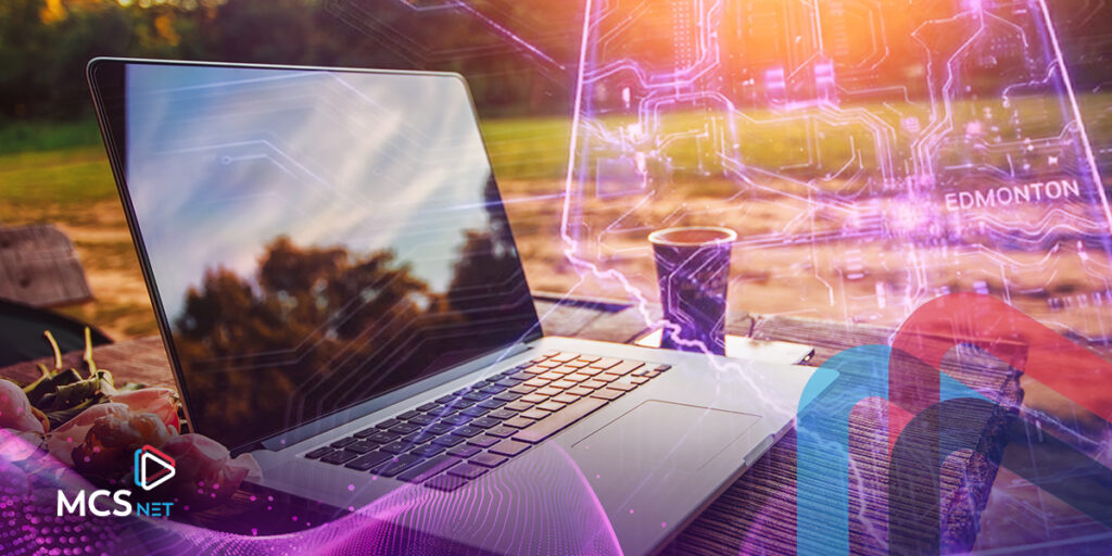 An outdoor photo with greenery in the background with a laptop computer in the foreground. There is a purple digital, transparent overlay of the map of Alberta.